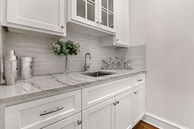 kitchen with a sink, backsplash, white cabinets, glass insert cabinets, and light stone countertops