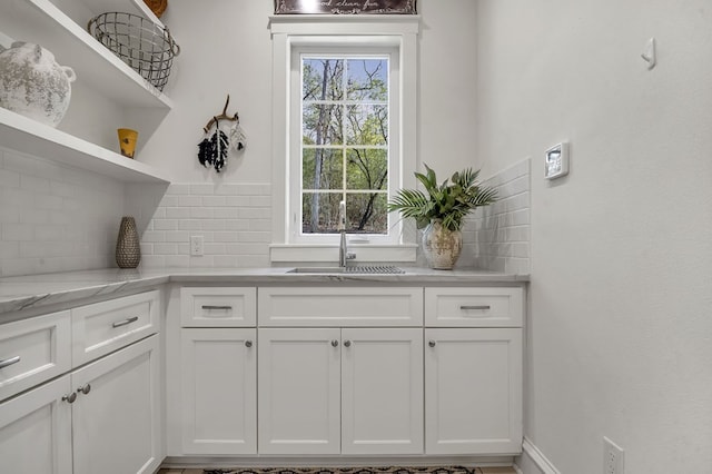 kitchen with a sink, open shelves, light stone counters, tasteful backsplash, and white cabinets