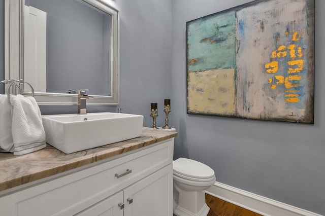 half bathroom with vanity, toilet, wood finished floors, and baseboards