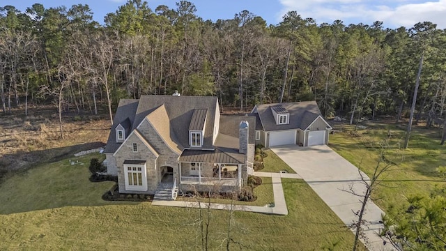 view of front of house featuring a front lawn, concrete driveway, metal roof, stone siding, and a standing seam roof