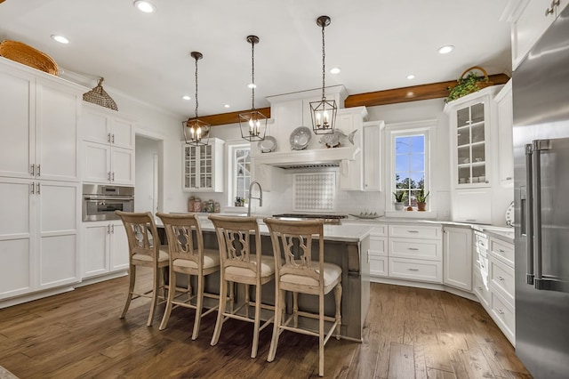 kitchen featuring a kitchen island with sink, stainless steel appliances, white cabinets, glass insert cabinets, and tasteful backsplash