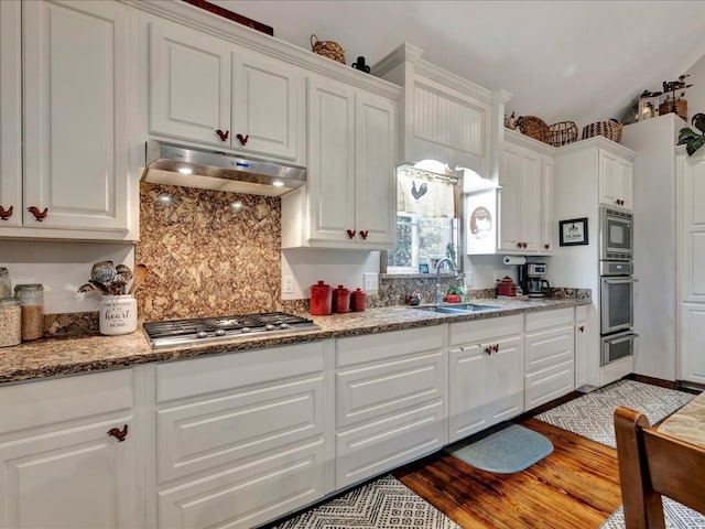 kitchen featuring decorative backsplash, appliances with stainless steel finishes, under cabinet range hood, white cabinetry, and a sink