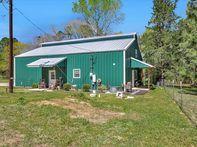 back of property with a pole building, an outbuilding, fence, metal roof, and a yard