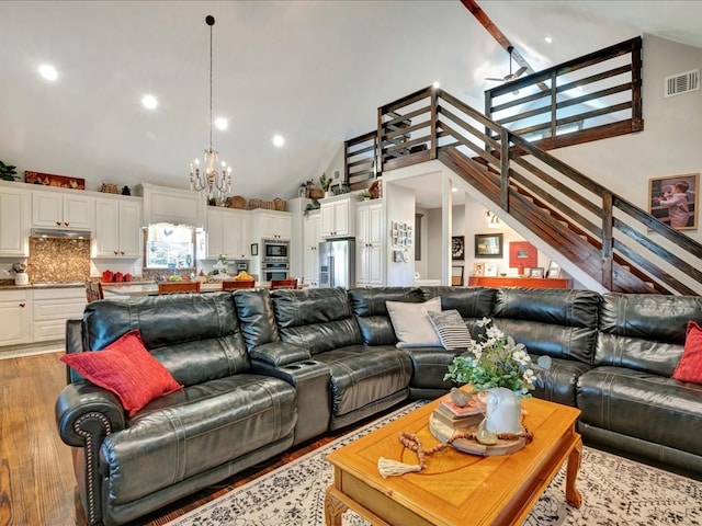 living area with high vaulted ceiling, stairway, a chandelier, light wood finished floors, and visible vents