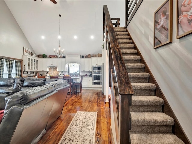 living room with dark wood-type flooring, high vaulted ceiling, stairway, and ceiling fan with notable chandelier