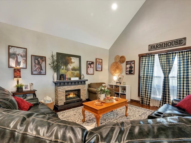 living room with a stone fireplace, high vaulted ceiling, and wood finished floors