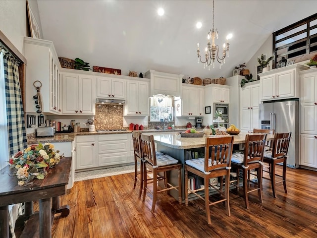 kitchen with white cabinetry, wood finished floors, a kitchen bar, under cabinet range hood, and stainless steel appliances