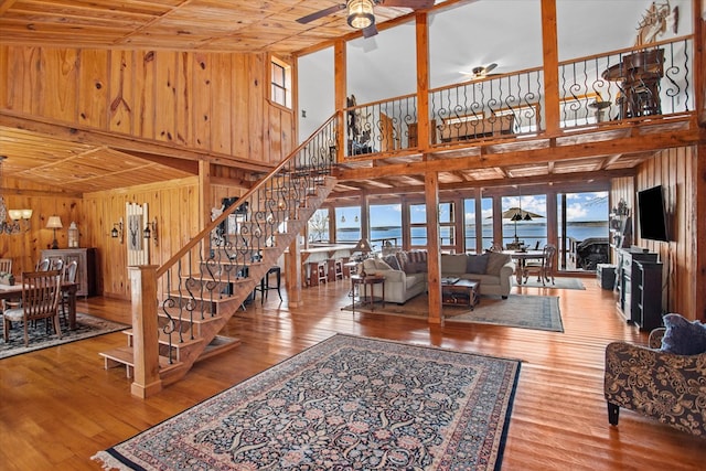 living area with wood walls, a wealth of natural light, stairway, and a ceiling fan