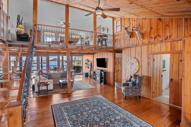 living room with wood walls, a towering ceiling, a ceiling fan, and wood finished floors