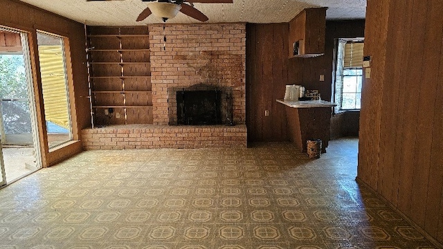 unfurnished living room featuring wooden walls, a fireplace, ceiling fan, and built in features