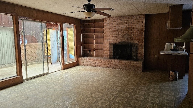 unfurnished living room featuring wooden walls, ceiling fan, built in features, a fireplace, and carpet floors