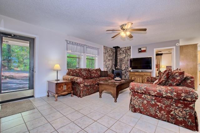 tiled living room with a textured ceiling, a wood stove, and ceiling fan