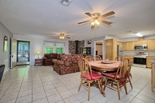 tiled dining space featuring ceiling fan, a wood stove, and a textured ceiling