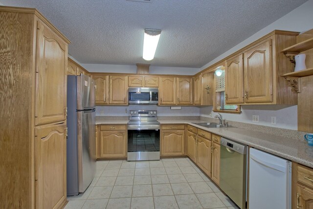 kitchen with a textured ceiling, sink, light tile patterned floors, and stainless steel appliances