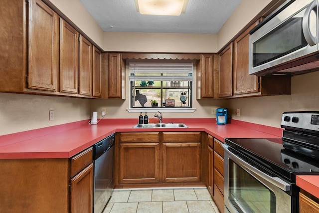 kitchen with light tile patterned floors, stainless steel appliances, a textured ceiling, and sink