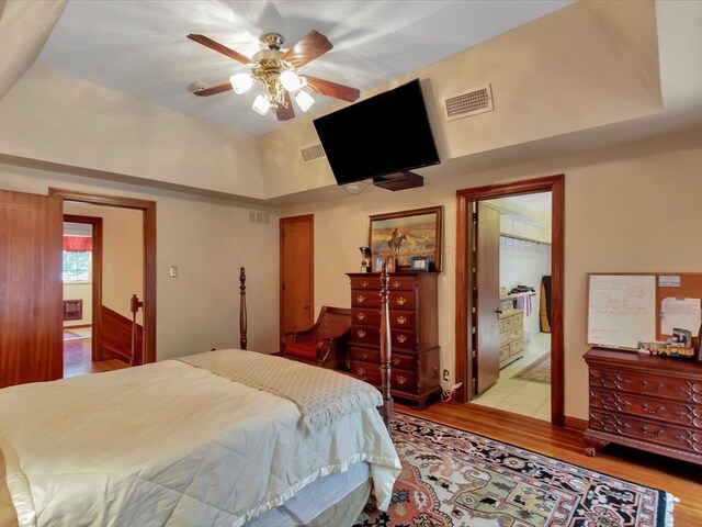 bedroom with a raised ceiling, connected bathroom, light hardwood / wood-style flooring, and ceiling fan