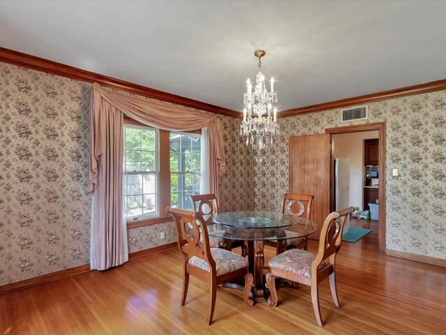 dining room with light hardwood / wood-style floors, ornamental molding, and a notable chandelier