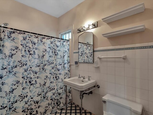 bathroom with toilet, tile walls, curtained shower, and sink