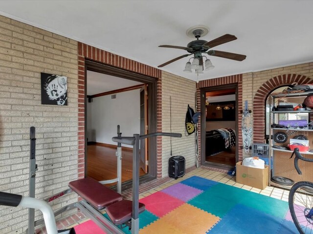 workout area with ceiling fan, crown molding, brick wall, and light hardwood / wood-style floors