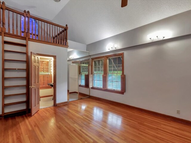 unfurnished living room featuring a textured ceiling, hardwood / wood-style flooring, and high vaulted ceiling