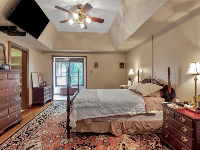 bedroom with a raised ceiling, access to exterior, ceiling fan, and light hardwood / wood-style flooring