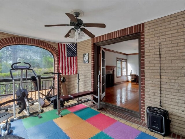 exercise area featuring ceiling fan, wood-type flooring, crown molding, and brick wall