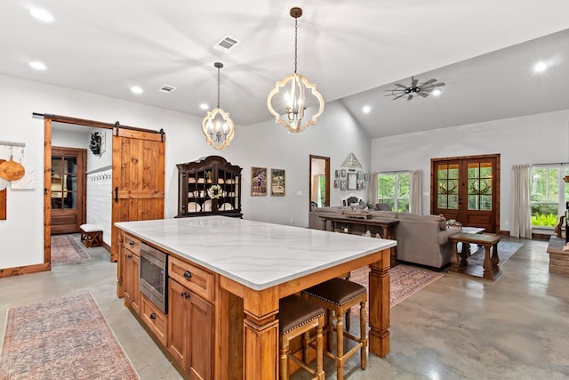 kitchen with light stone countertops, a barn door, decorative light fixtures, a center island, and stainless steel microwave