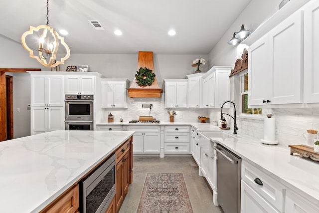 kitchen featuring light stone countertops, stainless steel appliances, a chandelier, pendant lighting, and white cabinets