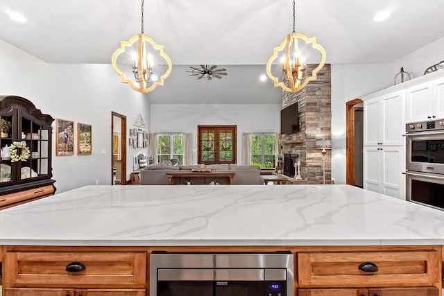 kitchen with pendant lighting, ceiling fan with notable chandelier, a fireplace, and appliances with stainless steel finishes