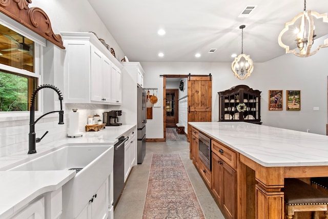 kitchen featuring sink, a barn door, appliances with stainless steel finishes, light stone counters, and white cabinetry