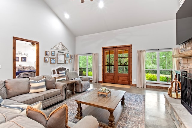 living room with a stone fireplace, ceiling fan, french doors, and high vaulted ceiling