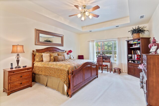 bedroom with a raised ceiling, ceiling fan, and light carpet