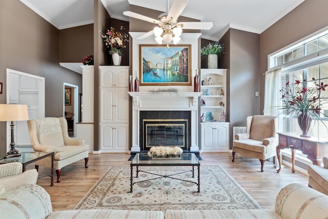 living room featuring crown molding, vaulted ceiling, ceiling fan, light wood-type flooring, and a tiled fireplace