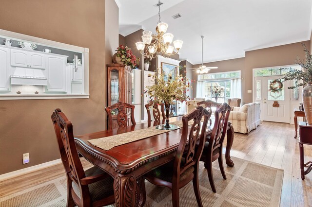 dining area with light hardwood / wood-style flooring, ceiling fan with notable chandelier, vaulted ceiling, and ornamental molding