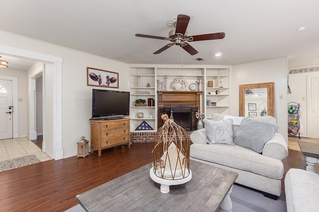 living room featuring ceiling fan, a fireplace, wood-type flooring, and built in features