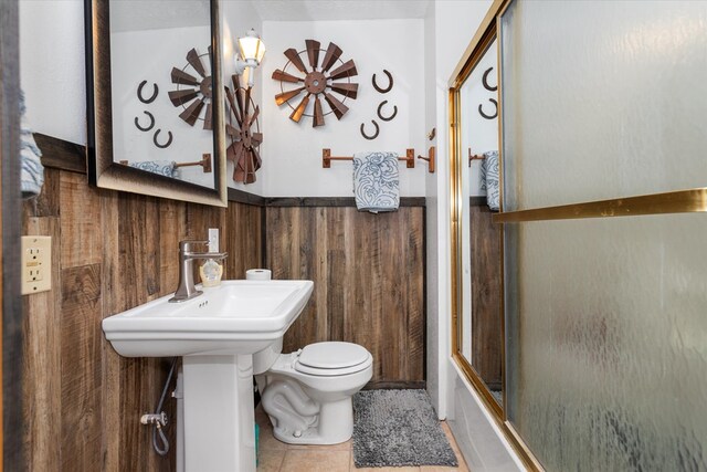 bathroom featuring combined bath / shower with glass door, tile patterned floors, toilet, and wooden walls