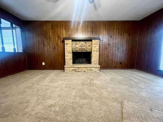 unfurnished living room featuring a brick fireplace, a textured ceiling, light colored carpet, ceiling fan, and wooden walls