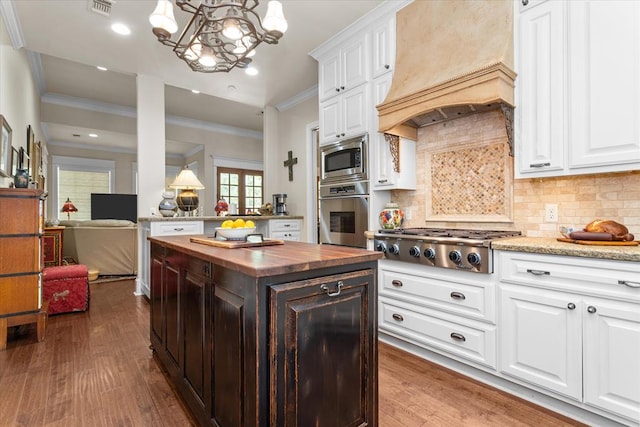 kitchen with ornamental molding, dark wood-type flooring, custom exhaust hood, and appliances with stainless steel finishes