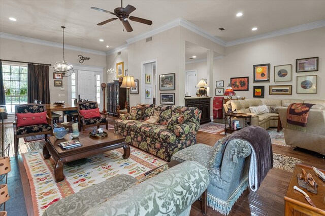 living room featuring crown molding, built in features, dark wood-type flooring, and ceiling fan with notable chandelier