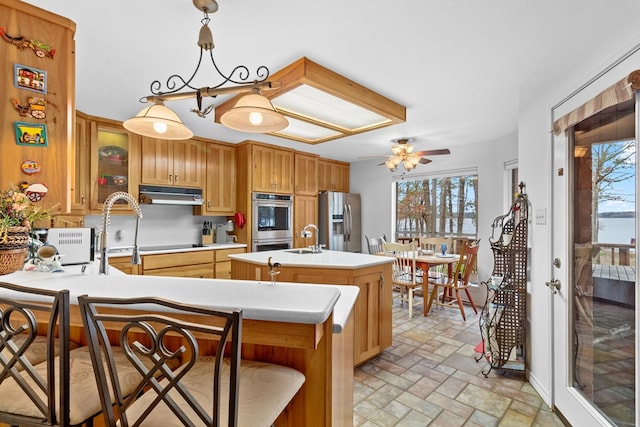 kitchen with ceiling fan, a center island with sink, hanging light fixtures, a kitchen breakfast bar, and stainless steel appliances