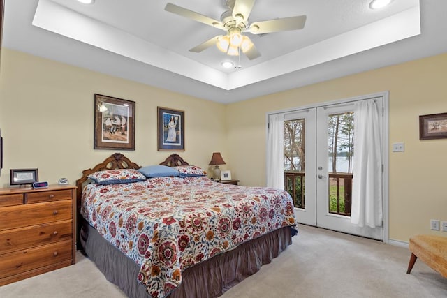 bedroom featuring light carpet, french doors, access to exterior, ceiling fan, and a tray ceiling