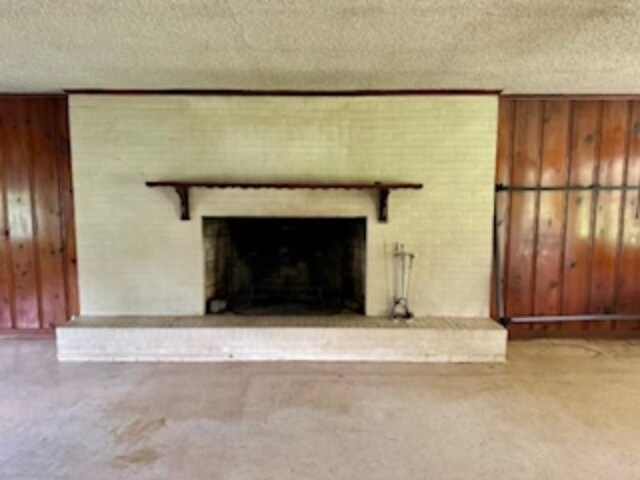 unfurnished living room featuring a fireplace, a textured ceiling, and wood walls