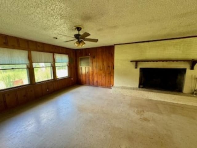 unfurnished living room with ceiling fan, a textured ceiling, wooden walls, and a brick fireplace