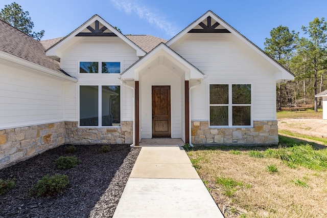 view of front of home featuring stone siding and roof with shingles