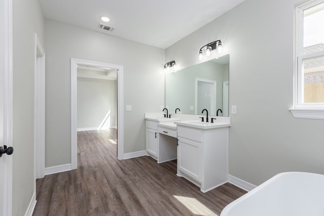 full bathroom with double vanity, visible vents, wood finished floors, a freestanding bath, and a sink