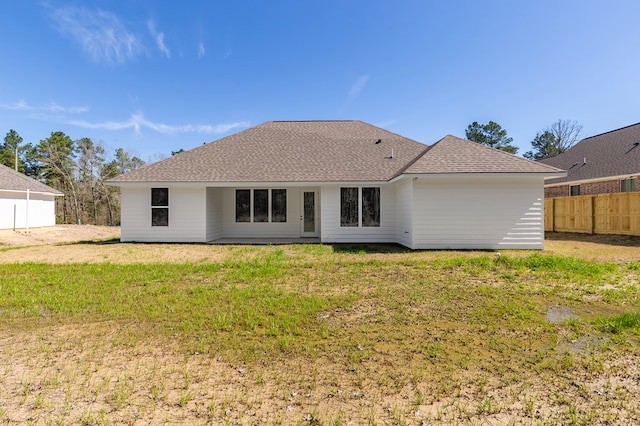 back of house featuring roof with shingles, a lawn, and fence