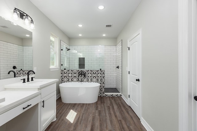 bathroom with visible vents, wood finished floors, vanity, a freestanding tub, and a walk in shower