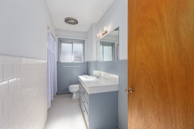 bathroom with tile patterned flooring, vanity, toilet, and tile walls