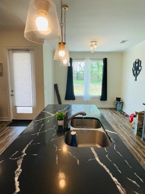 kitchen with dark wood-type flooring, dark stone counters, sink, ornamental molding, and decorative light fixtures