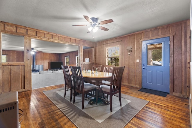 dining space with wood walls, a textured ceiling, and hardwood / wood-style flooring